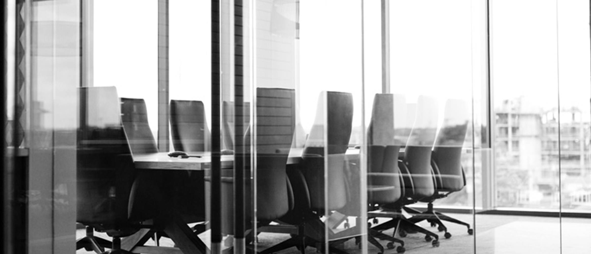 An empty black and white corner conference room that's in the corner of a office with windows looking out at buildings